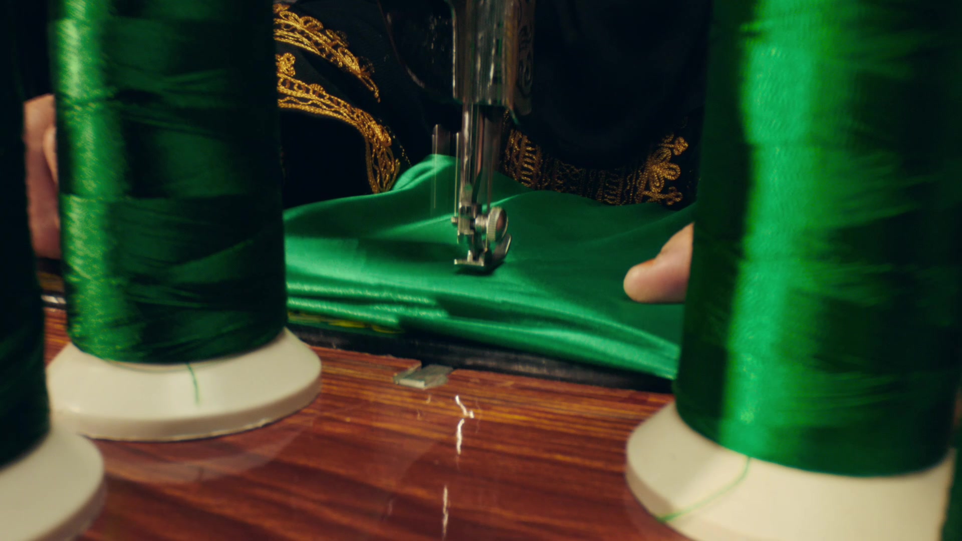 Green thread spools beside a sewing machine stitching the Saudi flag