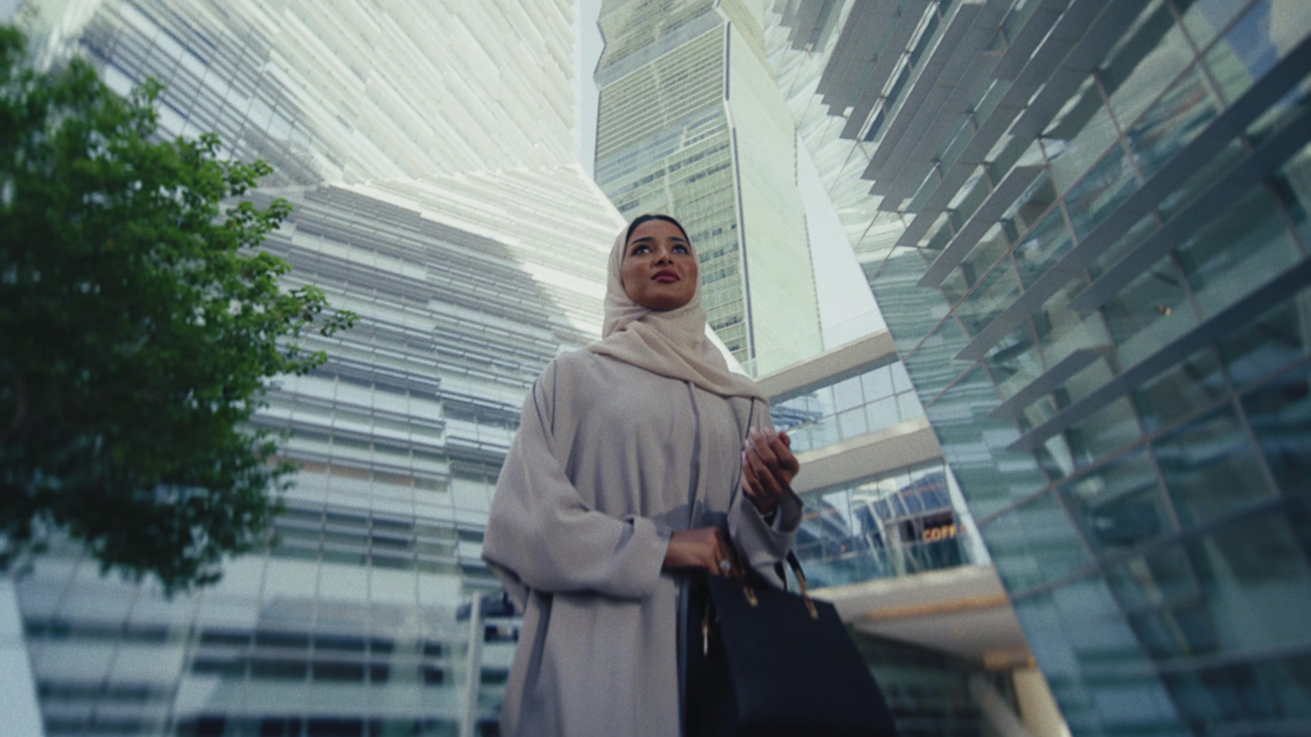 Woman in an abaya looking up between glass towers at KAFD