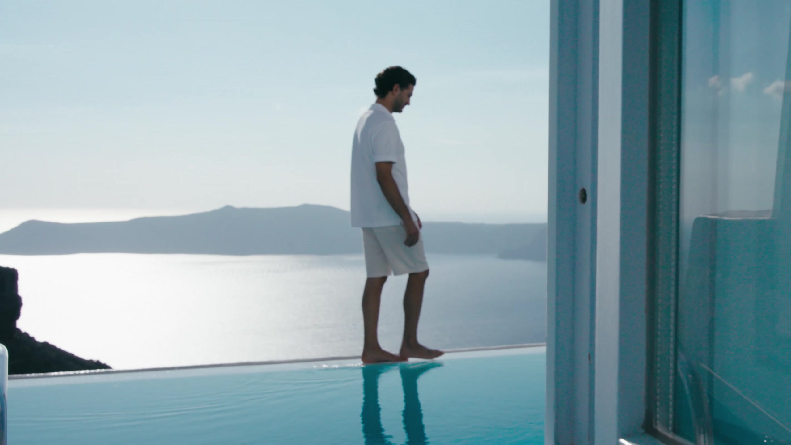 A man stands on the edge of an infinity pool above the caldera